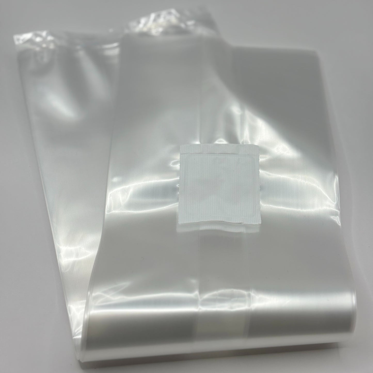 A stack of clear, Unicorn 10T oyster mushroom grow bags lie on a white floor. There is a 0.2 micron filter patch at the top of the bag for ventilation.