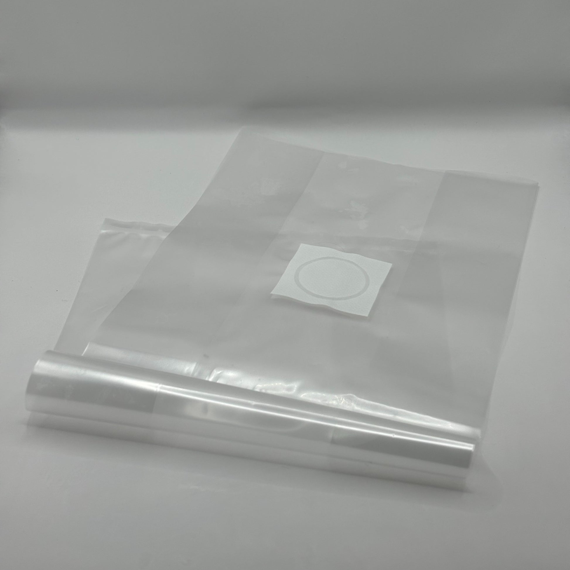 A stack of clear, oyster mushroom grow bags lie on a white floor. There is a 0.2 micron filter patch at the top of the bag for ventilation.